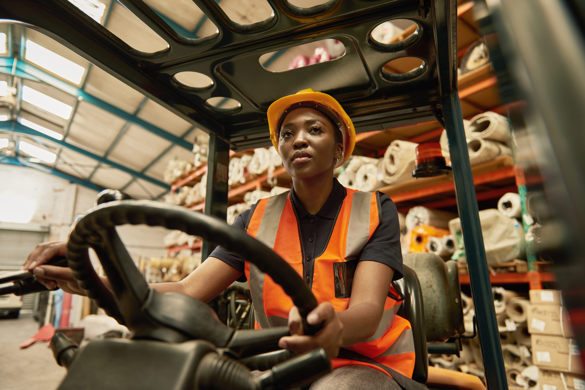 Young African female forklift operator driving around a warehouse class="lazyload